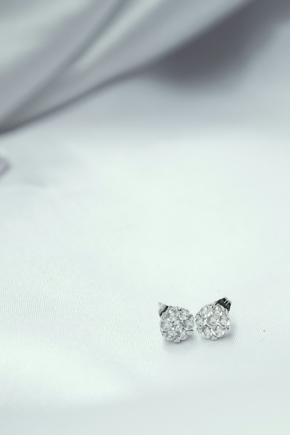 Due orecchini a grappolo d'argento appoggiati su tessuto bianco.