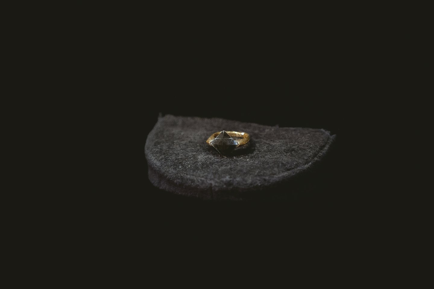 Un anello d'oro con una gemma scura è posato su un cuscino.