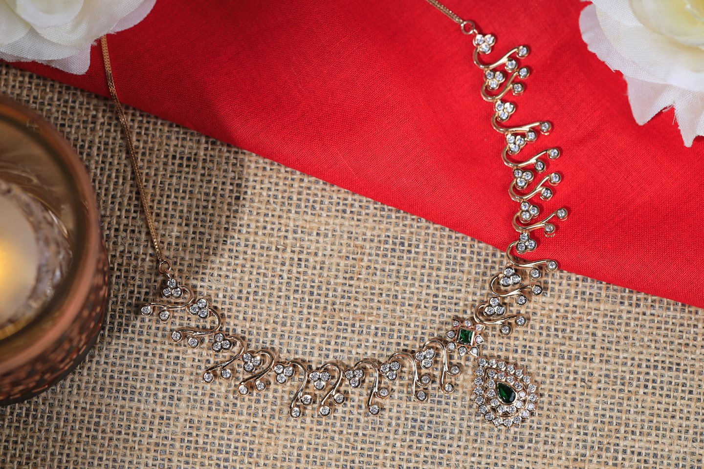 Collana d'oro con pietre su tessuto rosso e juta.