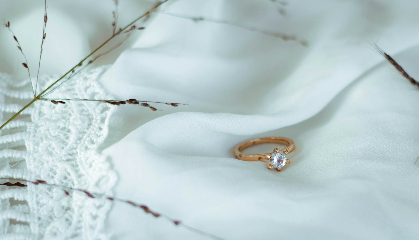 Un anello d'oro con una gemma trasparente posato su un tessuto bianco.