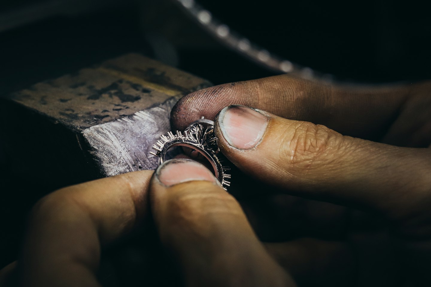 Mani di artigiano incastonano pietre in un anello d'argento su un banco da lavoro.